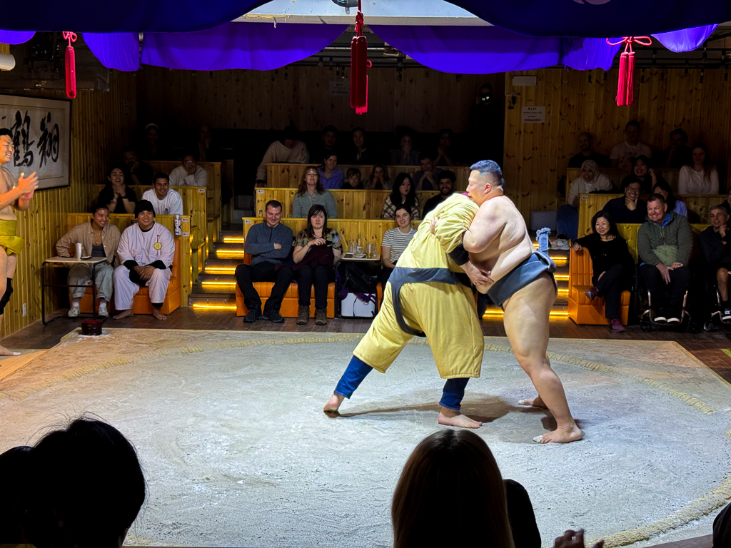 A volunteer attempting to wrestle a professional sumo wrestler at Asakusa Sumo Club in Tokyo.