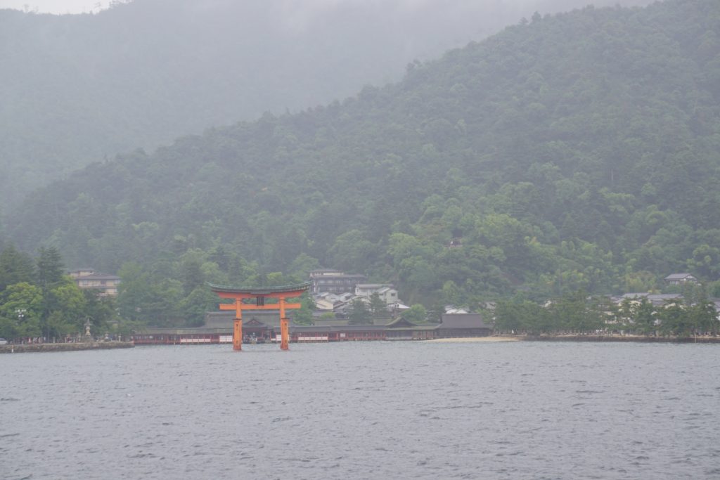 Foggy view of a mountain a orange torii gate, Itsukushima Shrine on Miyajima Island, Japan is in the foreground.