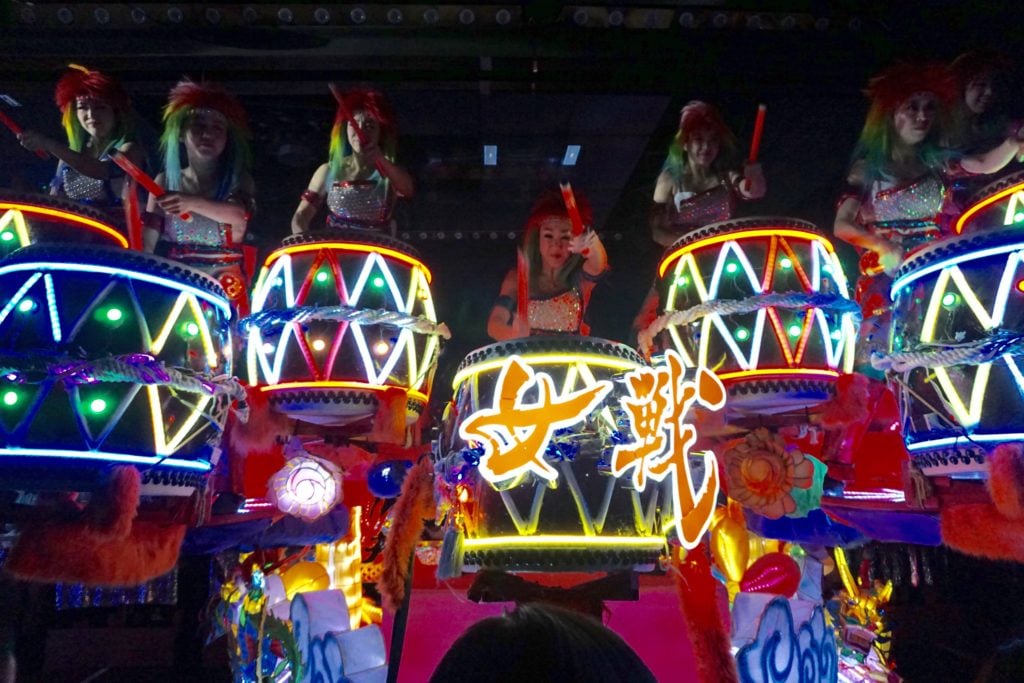 Girls playing drums that are lit up in multiple colors at the Robot Restaurant