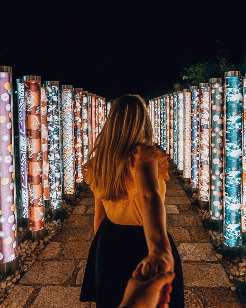 Girl walking through a path of illuminated colorful poles (Kimono Forest, Kyoto)