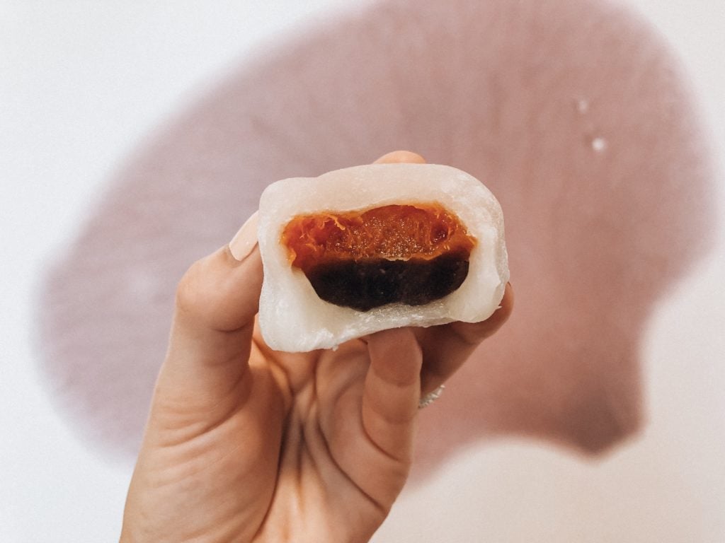 Hand holding a Japanese sweet called daifuku (a sweet rice flour dumpling filled with a layer of red bean paste and a dried apricot on top.