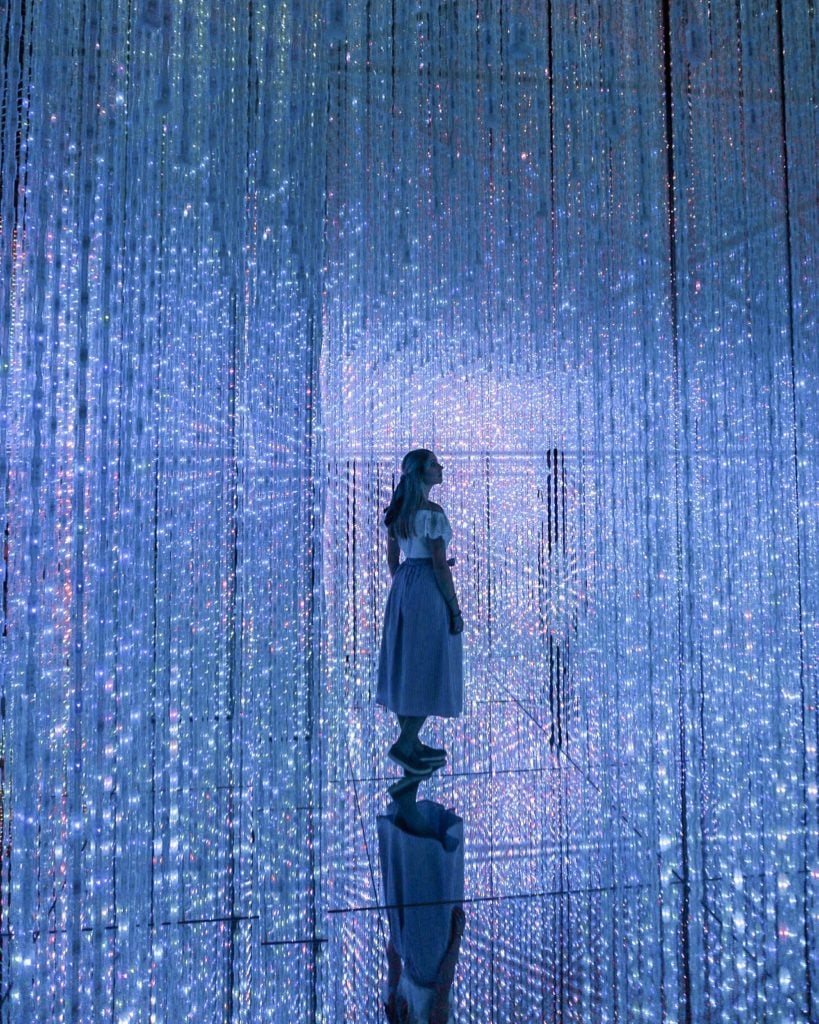 Girl standing in a room of blue lights from wall to ceiling - Mori Digital Art Museum Tokyo