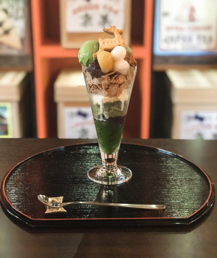 A matcha parfait with layers of jello, ice cream, cereal, mochi, and a biscuit shaped like a deer from Cafe Chaka in Nara, Japan