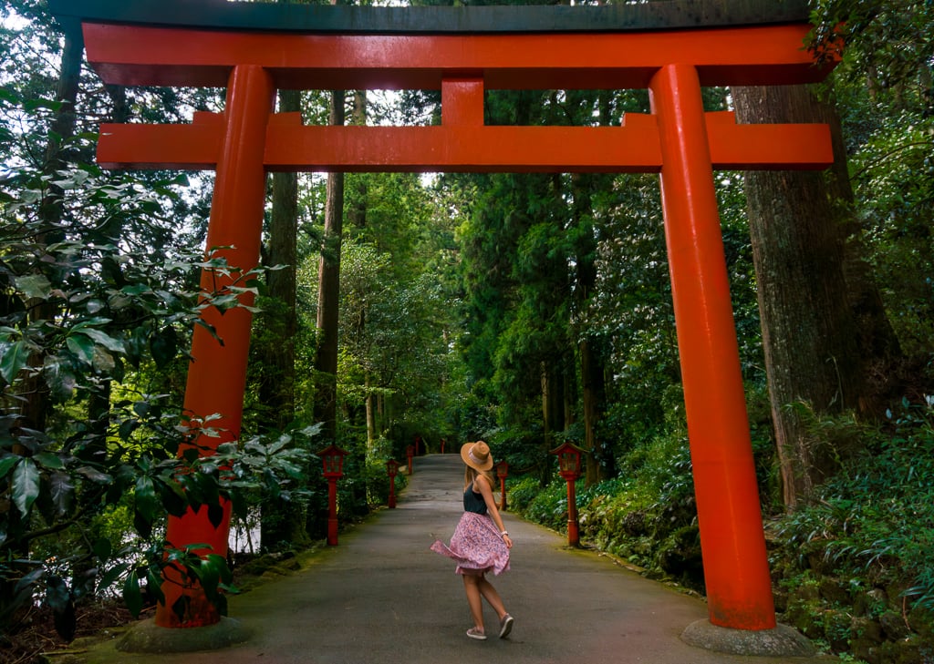 Entrance to Hakone Shrine marked by an vermillion color torii gate and surrounded by lots of green foliage.